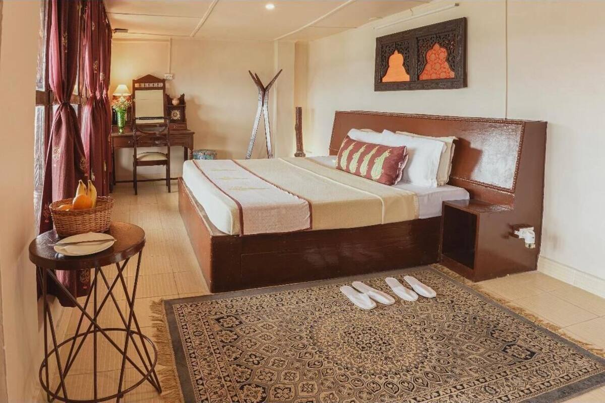 Habitación de hotel con una cama grande, un escritorio, una silla, una mesita con una cesta y un tapete estampado.
