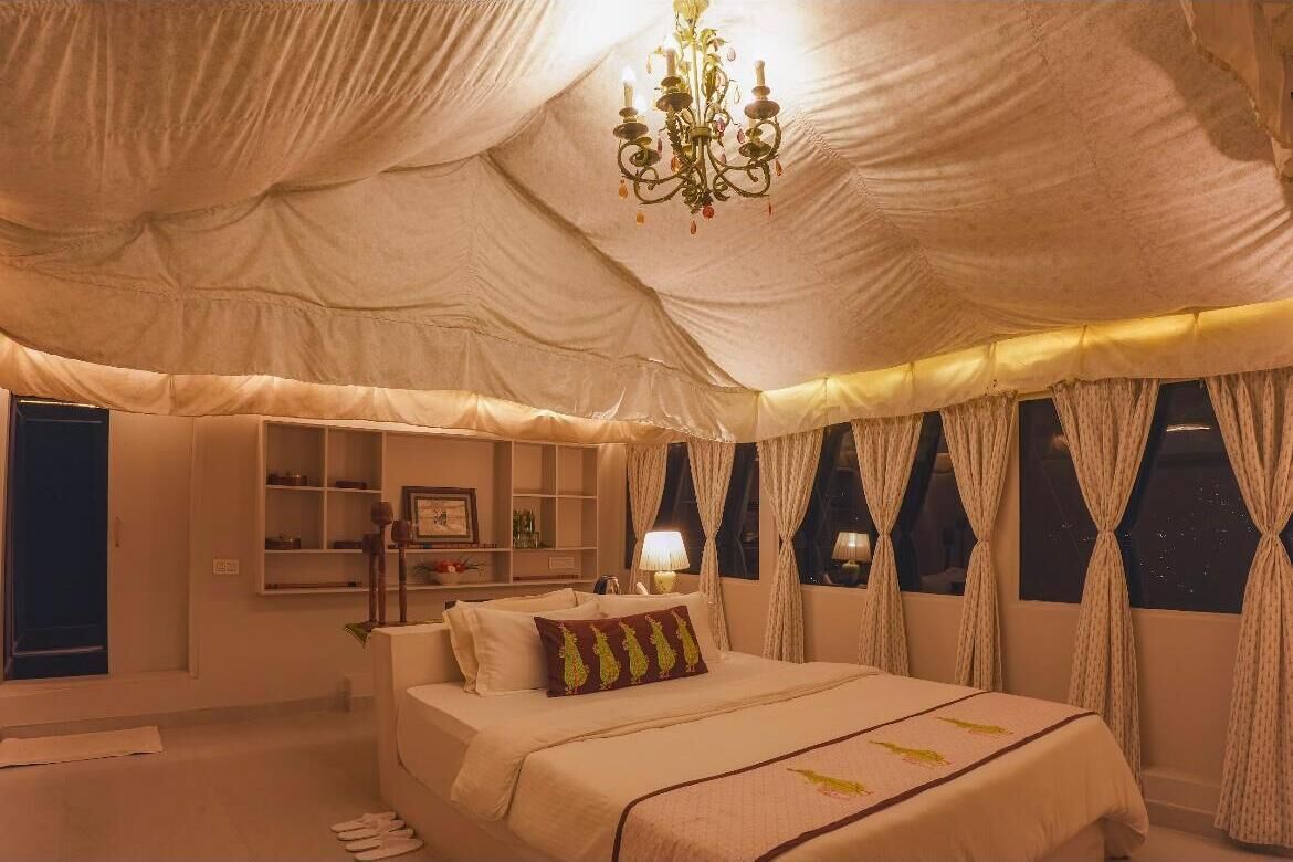 A tent-style bedroom with a bed, bedside tables, a lamp, and curtains.