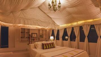 A tent-style bedroom with a bed, bedside tables, a lamp, and curtains.