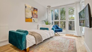 A bedroom with a bed, a blue armchair, a large window, and artwork on the wall.