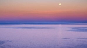 Ein ruhiges Meer bei Sonnenuntergang, mit sichtbarem Mond.