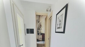 A narrow hallway with white walls and a light wooden floor. A door on the left leads to a room with a white radiator. A framed picture hangs on the right wall. - Lemon Suite - Prevo Cinque Terre (Vernazza)