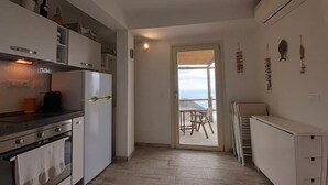 A modern kitchen with white cabinets, a stove, and an oven. There is a dining area with a table and chairs visible through an open door. - Lemon Suite - Prevo Cinque Terre (Vernazza)
