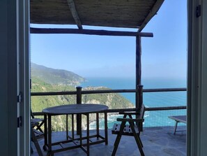 Ein Balkon mit Tisch und Stühlen, der Blick auf eine Küstenlandschaft mit Bergen und Meer freigibt.