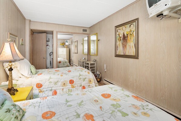 A hotel room with a bed, bedside table, lamp, mirror, and a painting on the wall.