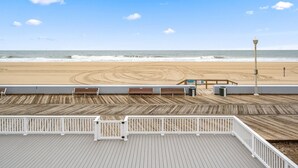 A beach view from a wooden deck with benches and a trash can.
