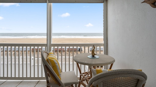 A balcony with wicker furniture, a view of the beach, and a white railing.