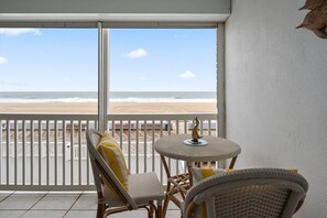 A balcony with wicker furniture, a view of the beach, and a white railing.