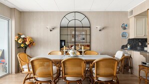 A dining room with a large table, wicker chairs, a vase of flowers, and a kitchen area with a black countertop.