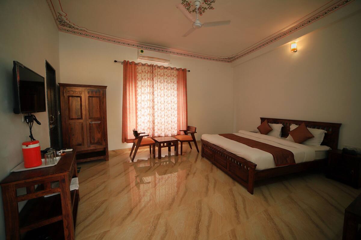A bedroom with a bed, a desk, a chair, a television, and an air conditioning unit.