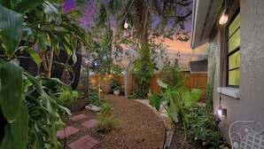 A garden pathway with mulch and stepping stones, surrounded by various plants and a wooden fence.