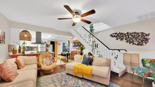 A spacious living room with a beige sofa, a colorful rug, and a ceiling fan.