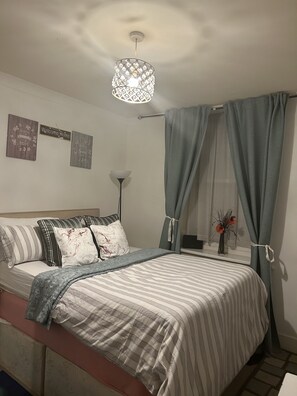 Ein ordentlich bezogenes Bett mit gestreifter Bettwäsche, eine Nachttischlampe und zwei Wanddekorationen.