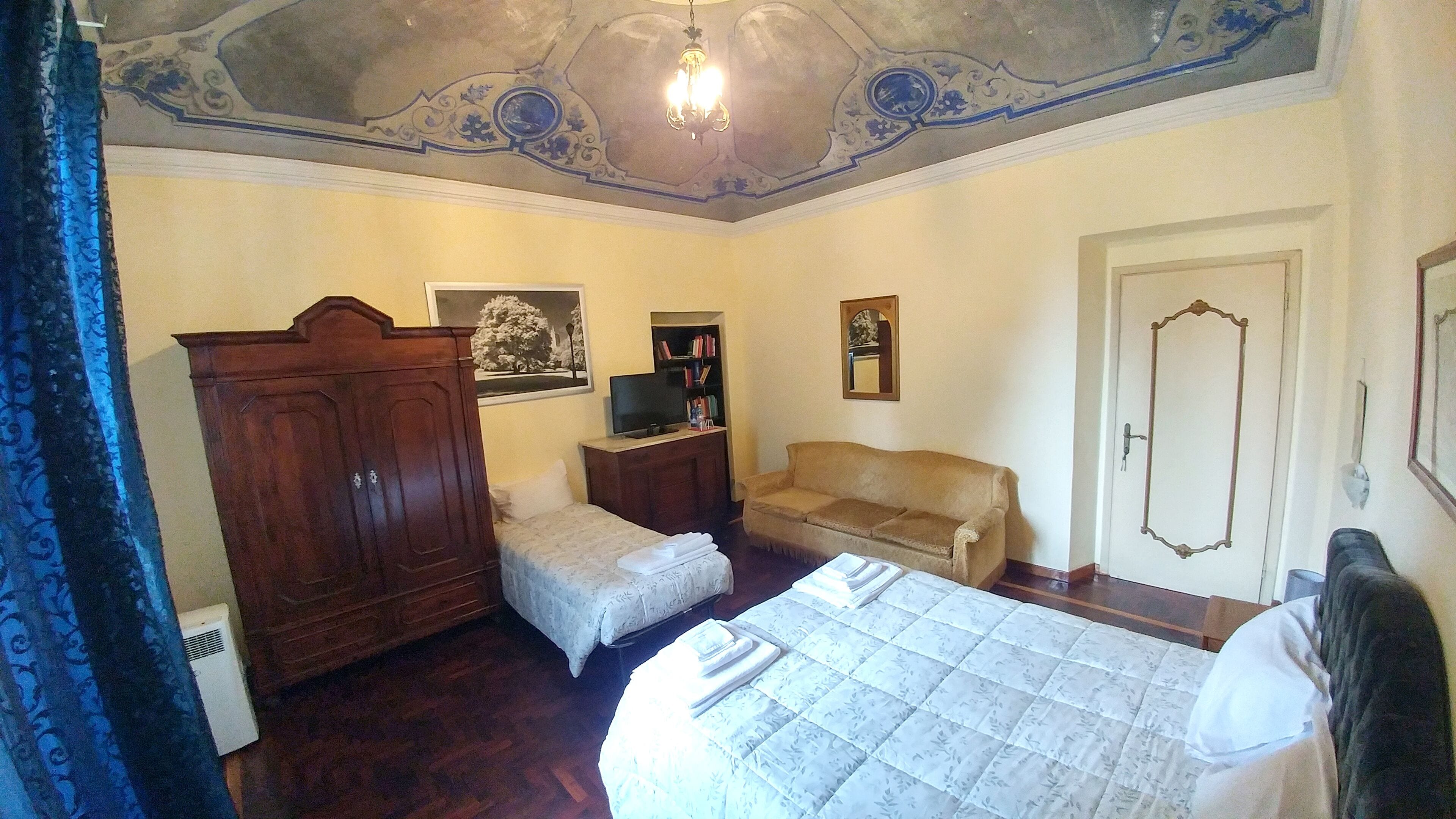 A bedroom with a bed, a wooden wardrobe, a sofa, a television, and a door.