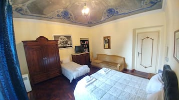 A bedroom with a bed, a wooden wardrobe, a sofa, a television, and a door.