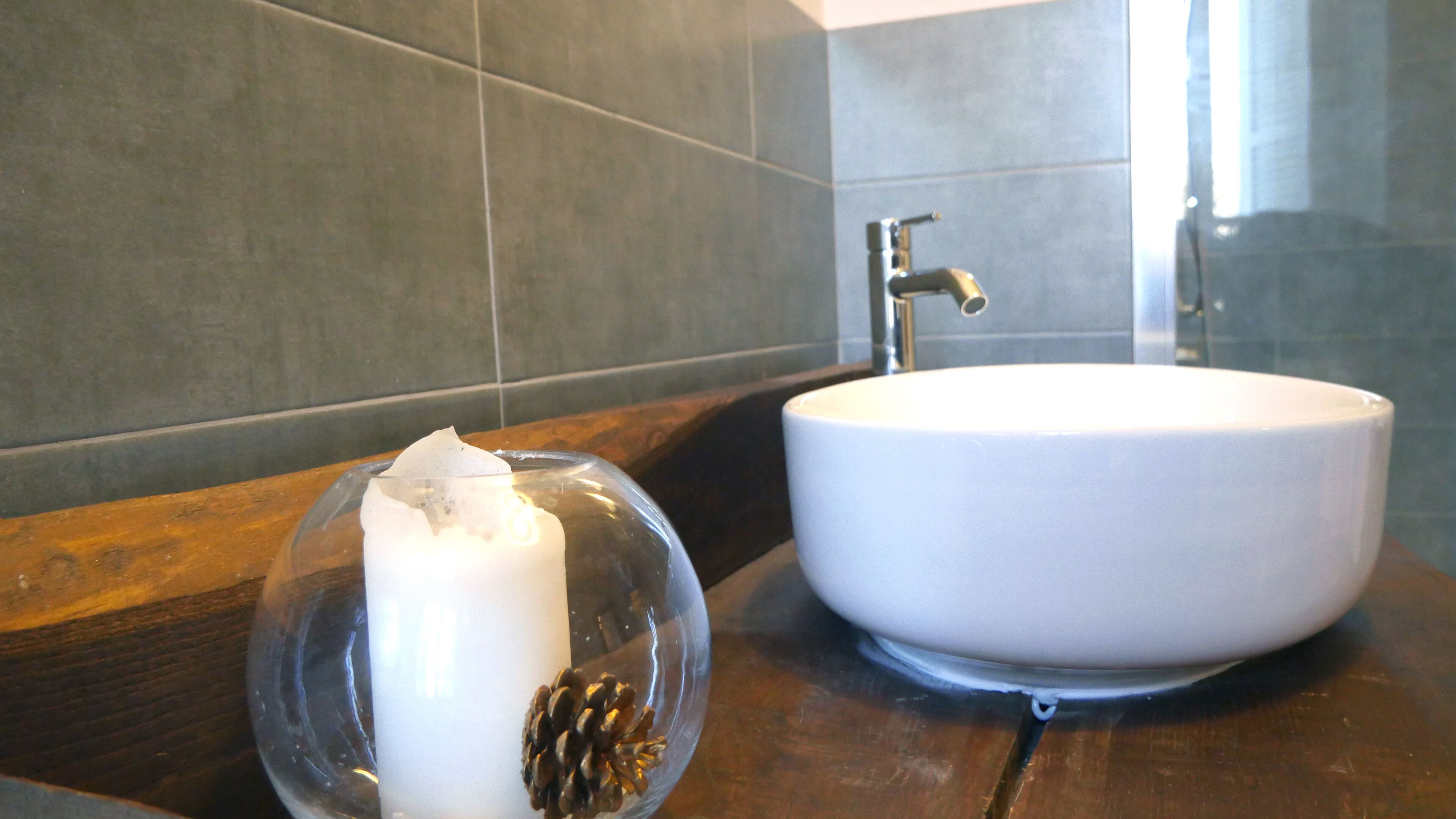 Une salle de bain avec un lavabo blanc, un plan de toilette en bois foncé et des murs carrelés.