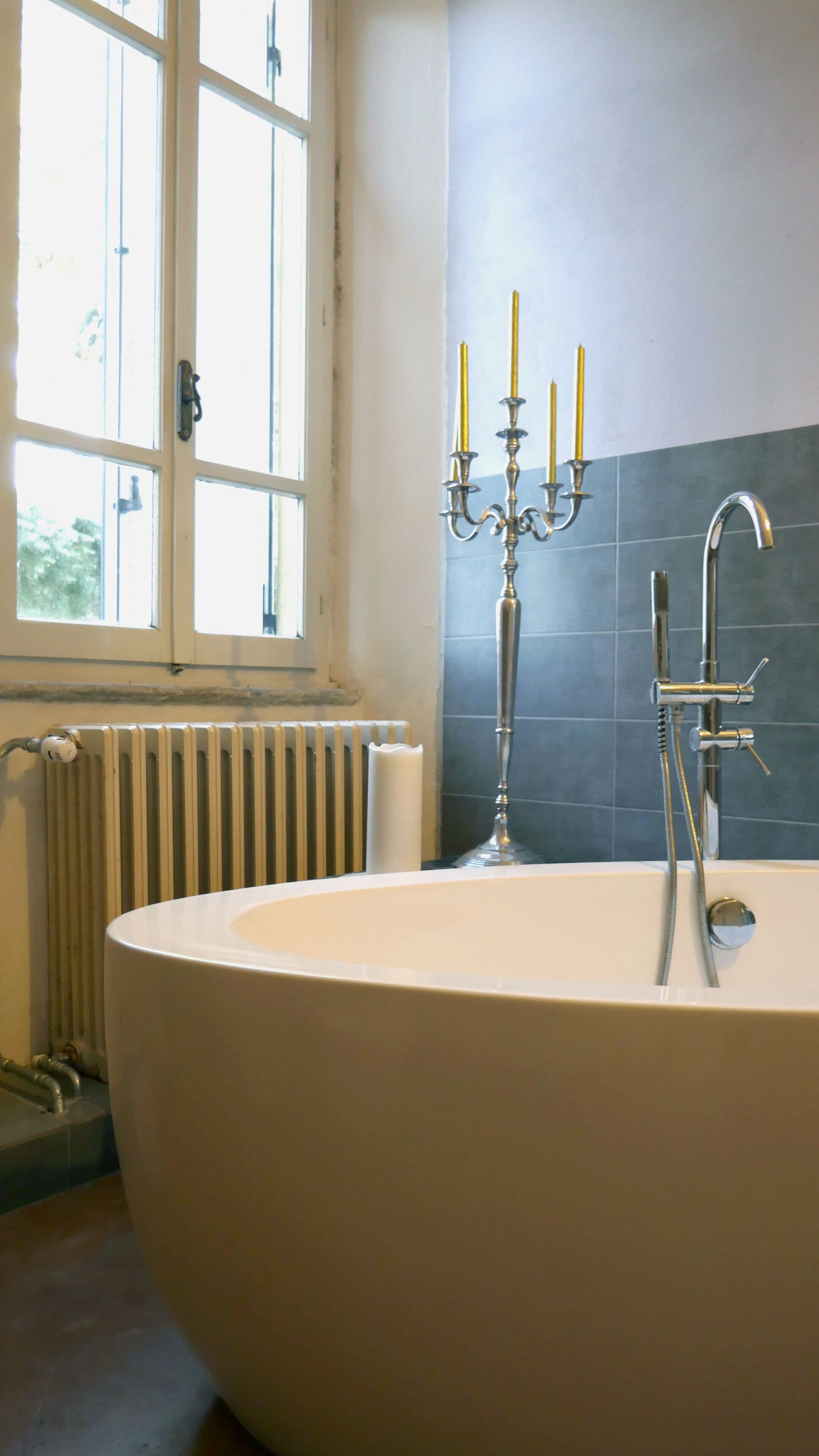 A modern bathroom with a freestanding bathtub, a window with a view, a radiator, and a candelabra with candles.