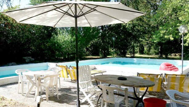 A pool area with a table and chairs, a red inflatable ring, and an umbrella. - Bresbot (Bressana Bottarone)