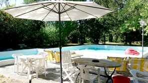 A pool area with a table and chairs, a red inflatable ring, and an umbrella. - Bresbot (Bressana Bottarone)