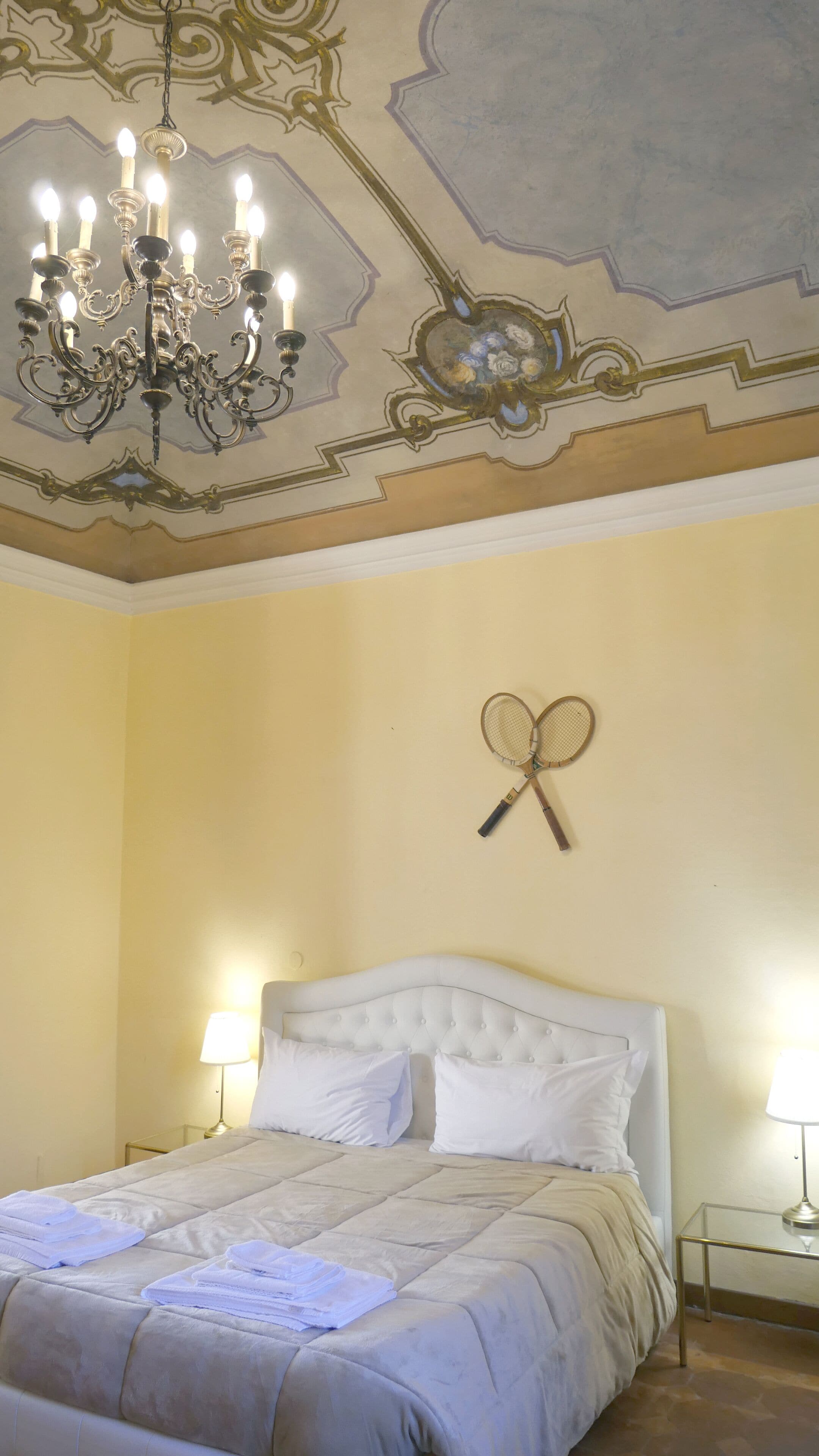 A bedroom with a large bed, a chandelier, and two wall-mounted tennis rackets.