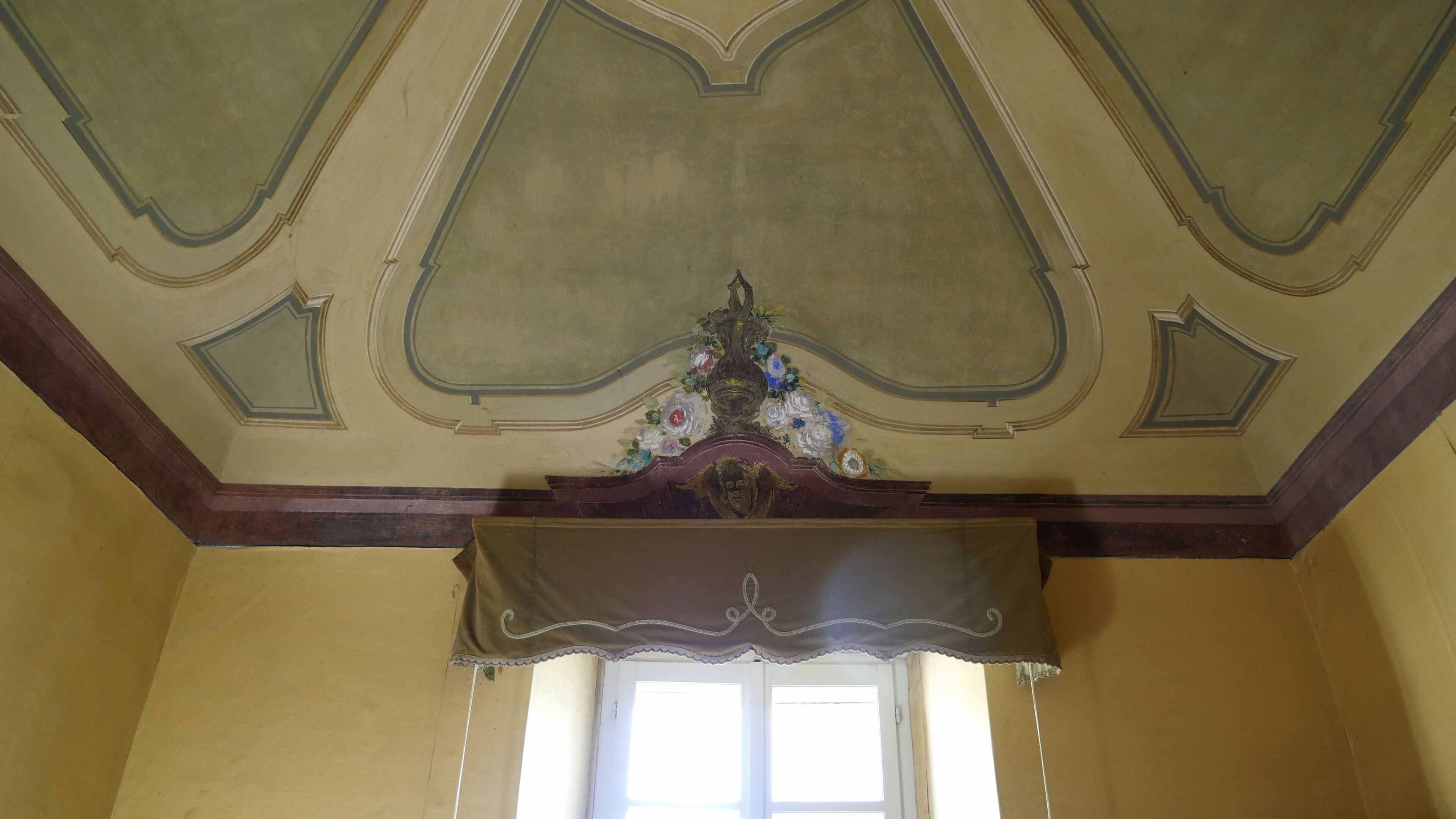 Una habitación con un techo alto y ornamentado y un panel de madera decorativo debajo de una ventana.
