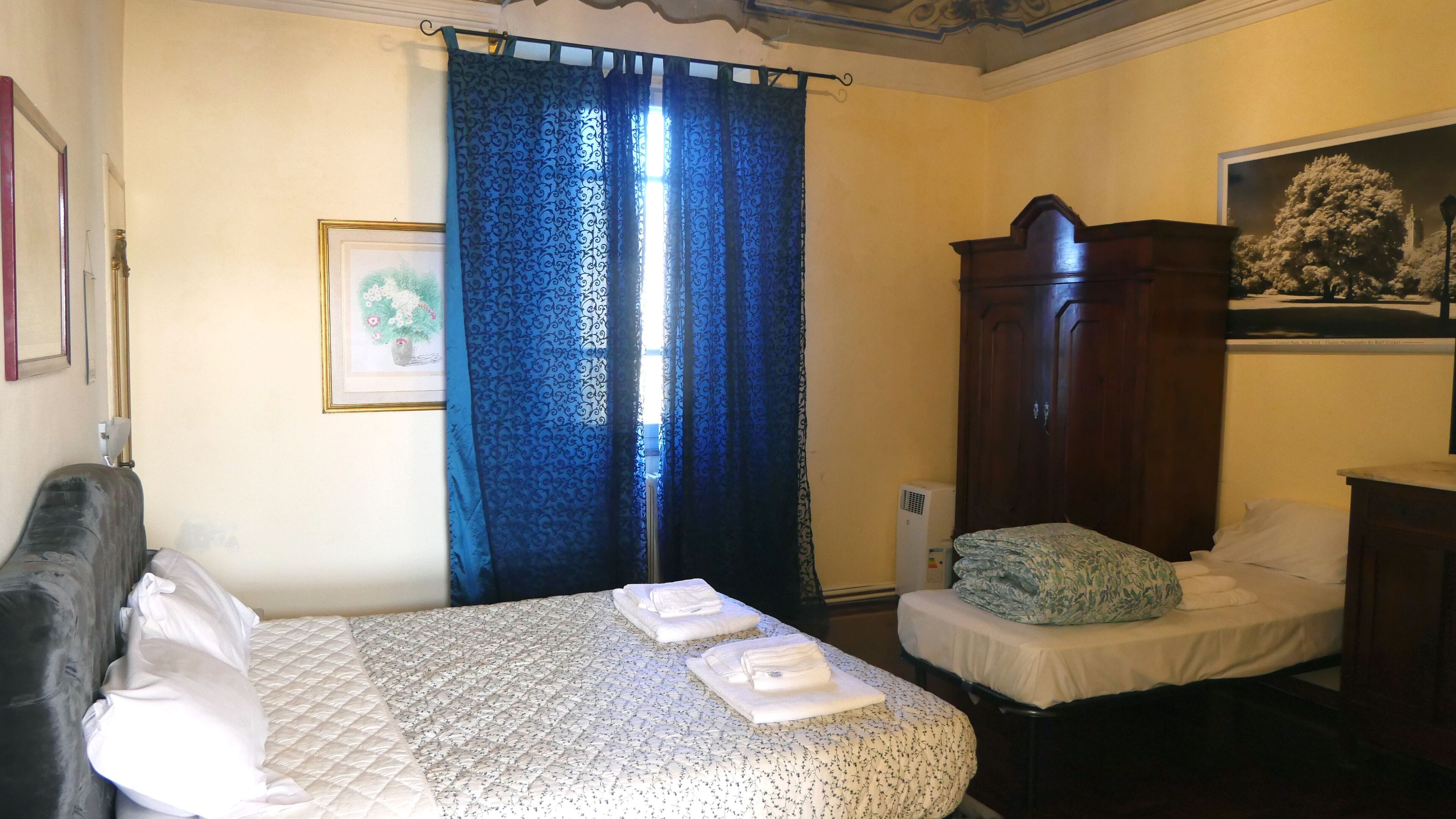 A room with a bed, a smaller bed, a wardrobe, and a framed picture on the wall.