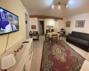 En stue med TV, spiseområde og køkken i baggrunden.