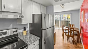 Cozinha moderna com eletrodomésticos de aço inoxidável, bancada de granito e área de jantar com mobiliário de madeira.