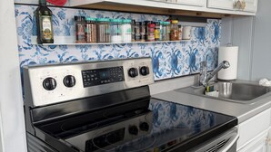 Una cocina con estufa negra, armarios blancos y salpicadero con motivos florales azules.