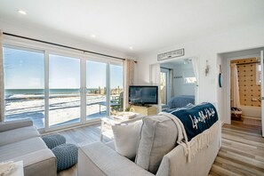 Enjoy the stunning view of the beach and sea from this spacious living room with a large window, comfortable sofa, and television.