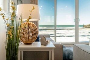 Enjoy a serene sea view from the comfort of this stylish room, featuring a large window, a table with a lamp and vase, and a decorative fish sculpture.