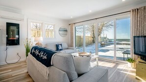 A modern living room with a large gray sofa, a flat-screen TV, and a view of a snowy outdoor area. - Wait 'n Sea Lake house near Point Pelee (Leamington)