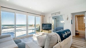 A spacious living room with large windows overlooking a beach, a television, and a cozy seating area. - Wait 'n Sea Lake house near Point Pelee (Leamington)
