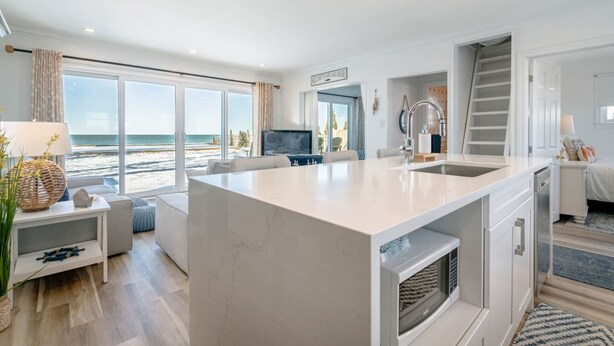 A modern kitchen with a central island, a dining area with a view of the beach, and a living room with a television. - Wait 'n Sea Lake house near Point Pelee (Leamington)