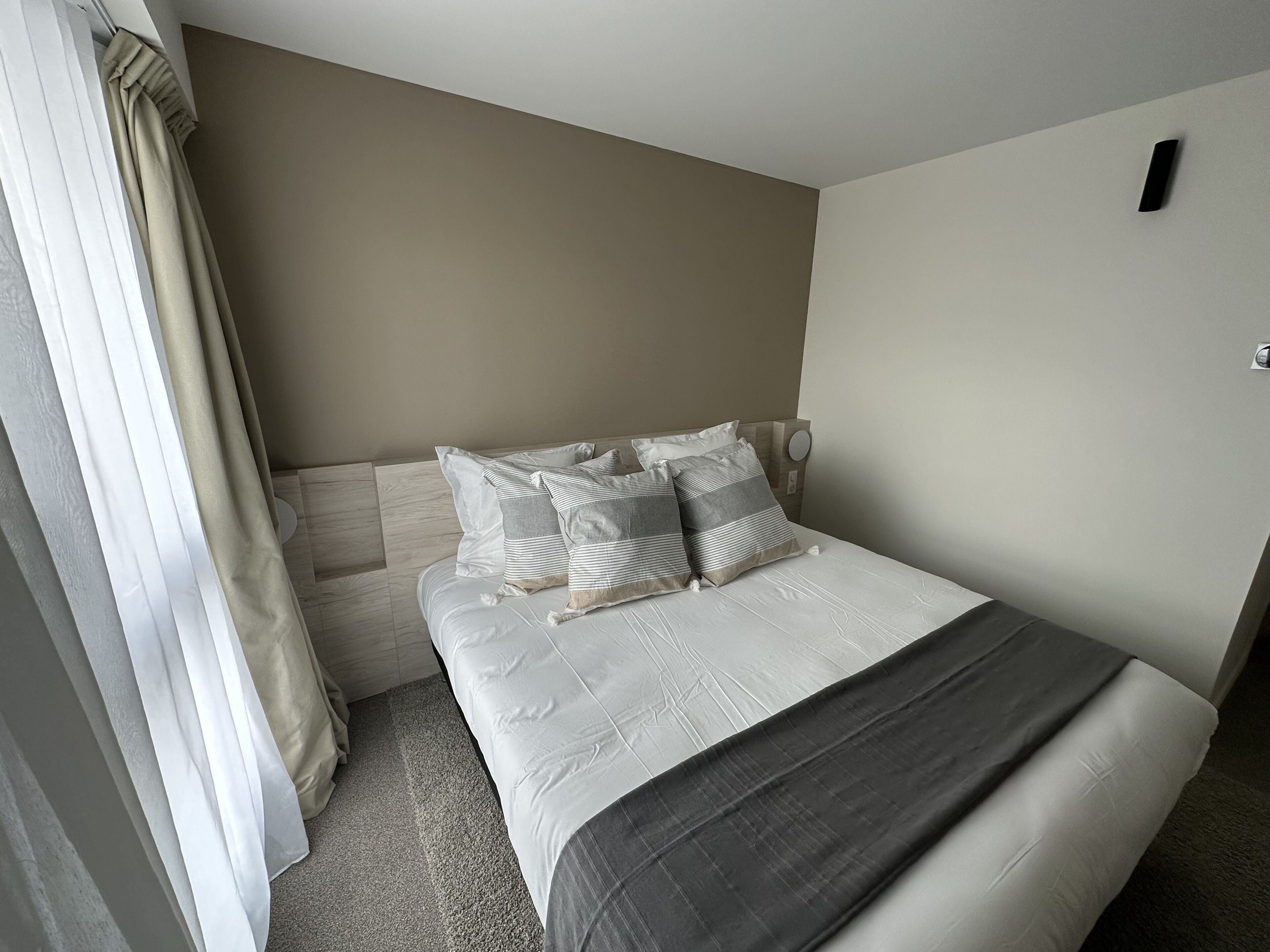 Una cama bien hecha con un juego de almohadas a rayas gris y blanco, una manta gris oscuro y un cabecero de madera.