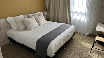 Una cama bien hecha con una manta gris, almohadas blancas y un cabecero frente a una pared amarilla.