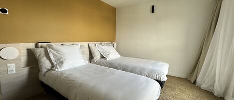 A hotel room with two beds, a wooden headboard, a round light fixture, and a power outlet.
