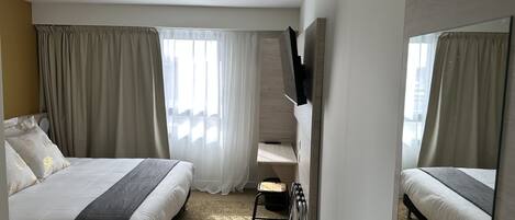 A hotel room with two beds, a large mirror, a flat-screen TV, and a small table.
