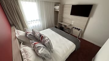 Una habitación de hotel con una cama, televisor montado en la pared, una mesita y una silla.