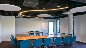 Sala de conferências com uma mesa comprida, cadeiras azuis e luminárias modernas.
