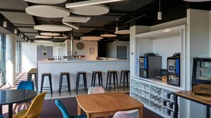 Uma área de bar moderna, com mesas redondas, banquetas e um balcão com uma máquina de café.