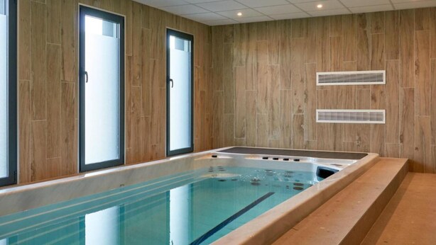 Piscina interna moderna com paredes de painel de madeira, amplas janelas e ar condicionado integrado.
