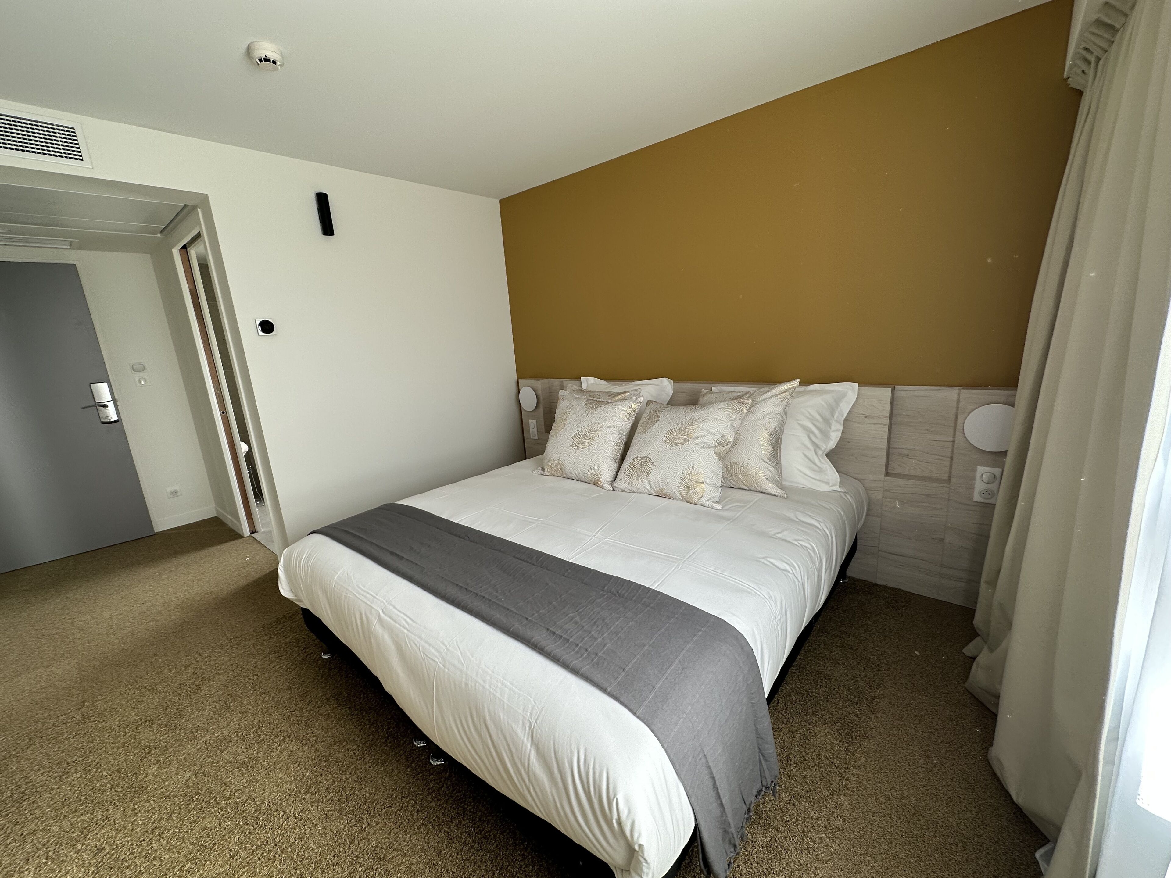 Een hotelkamer met een bed, een deur en een muur met een lichtschakelaar.