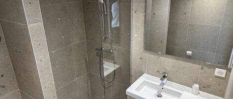 Un baño moderno con ducha de vidrio, lavamanos blanco y espejo sobre él.