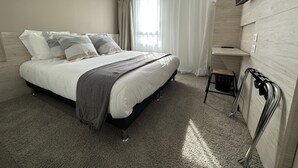 Quarto de hotel moderno com uma cama grande, televisão na parede e uma pequena área de estar.