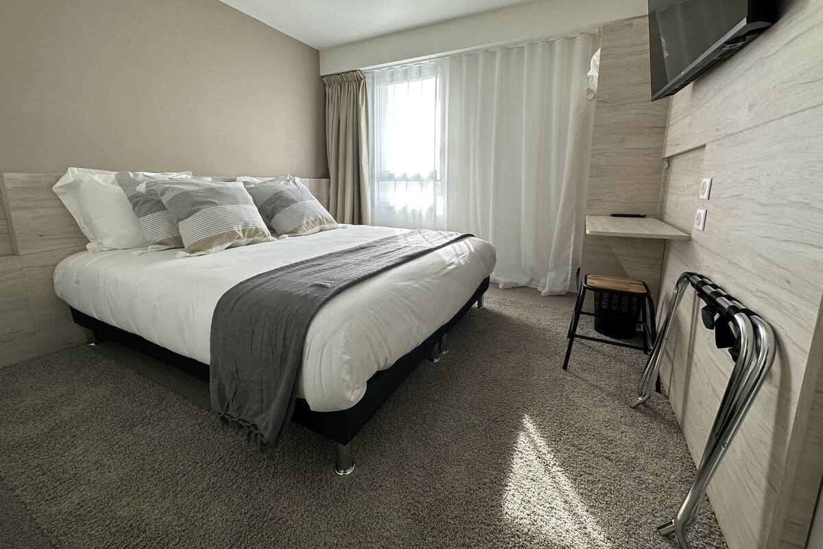 Una habitación de hotel moderna con una cama grande, un televisor montado en la pared y una pequeña zona de estar.