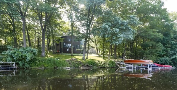 Ein Seehaus, umgeben von dichtem Wald, mit einem Steg und einem roten Boot.