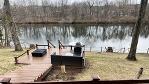 A wooden deck with outdoor seating and a view of a calm lake surrounded by trees.