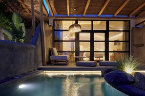 Un área de piscina interior moderna con techo de madera, una lámpara colgante y un espacio de estar con vistas a la piscina.
