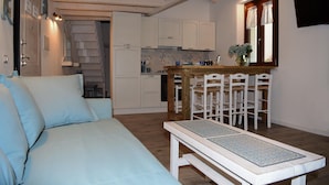 Una camera da letto con un letto, una panca e un piccolo tavolo da pranzo con sedie. C’è un angolo cottura con mobili e un fornello.